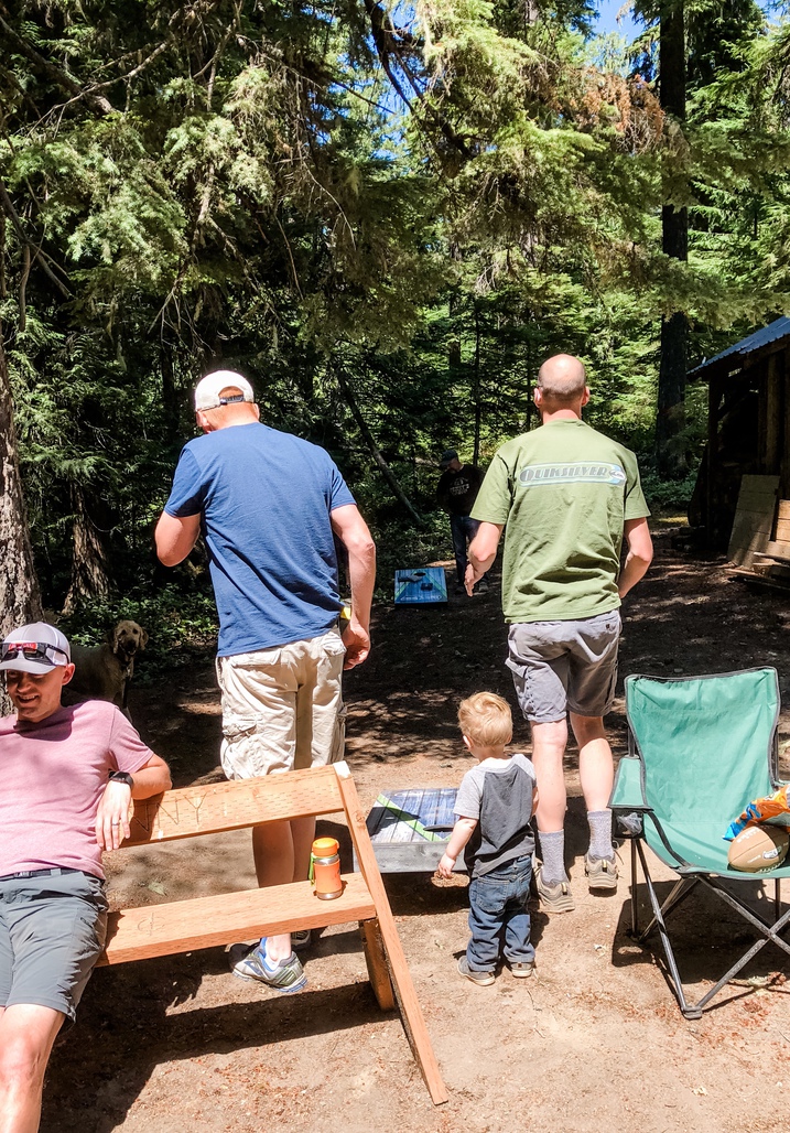 men and toddler boy play game of bags in woods at cabin