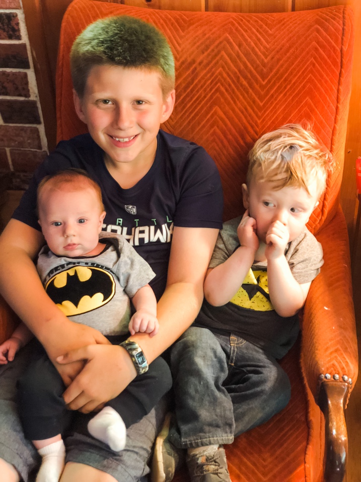 older cousin holds baby cousin and toddler boy in chair inside cabin