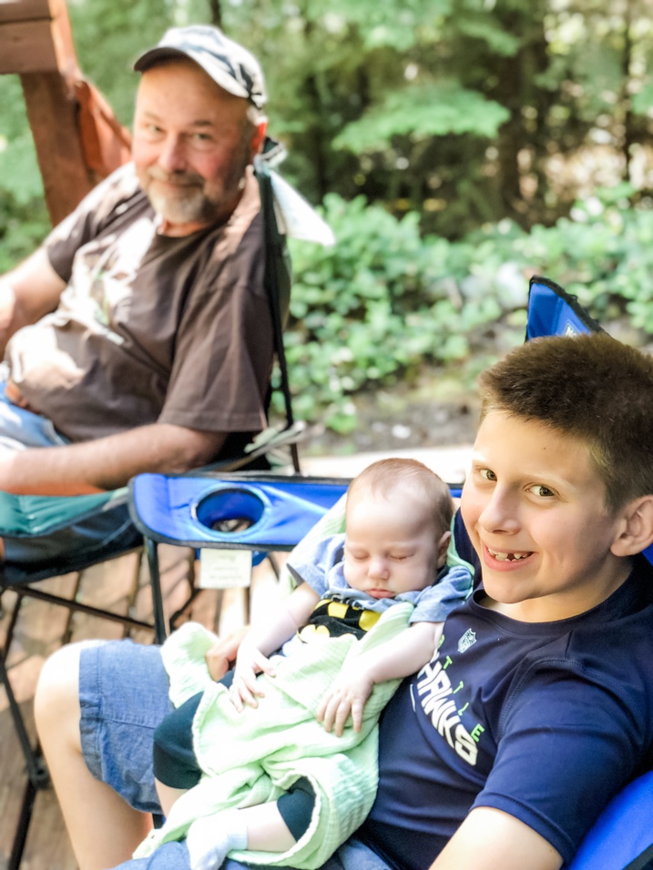 boy holds baby cousin with grandpa in background