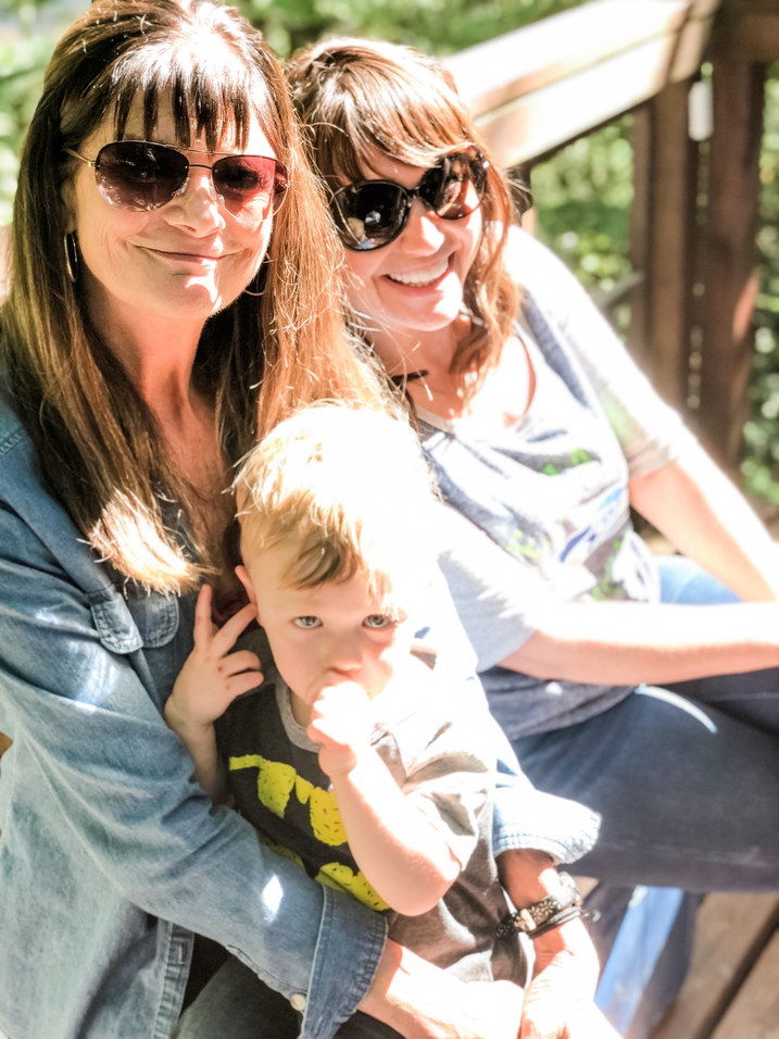 a grandmother holds her toddler grandson with her daughter sitting next to her